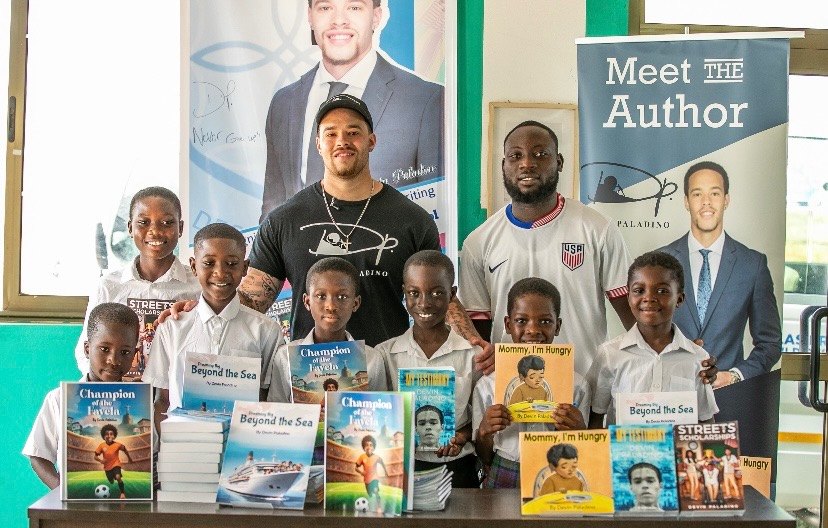 A “Meet the Author” display in Tema, Ghana, with pupils standing behind a table of Devin Paladino’s books
