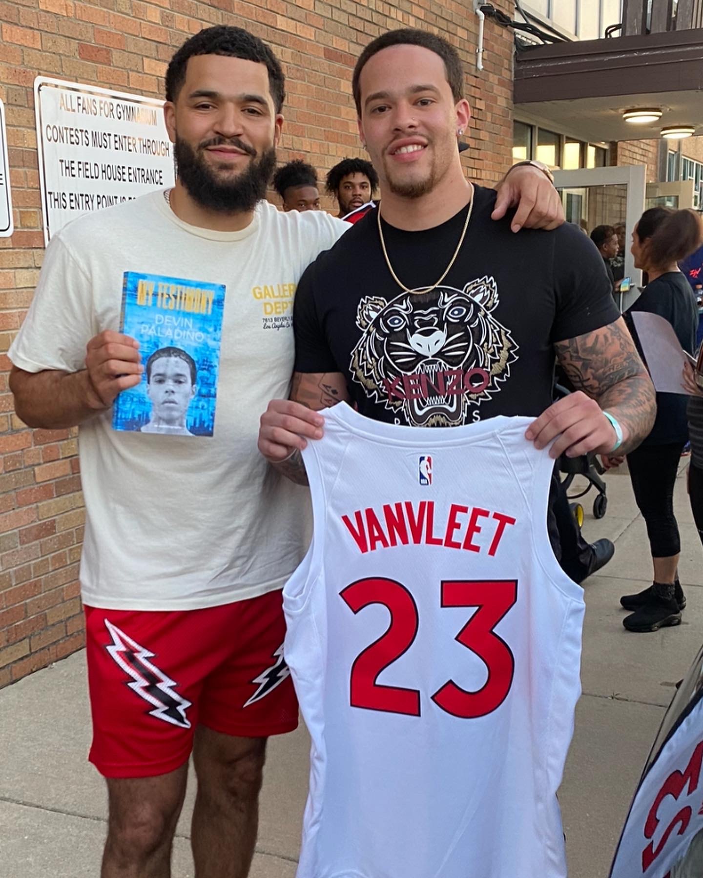Devin Paladino with an athlete holding a signed number 23 jersey and a copy of My Testimony