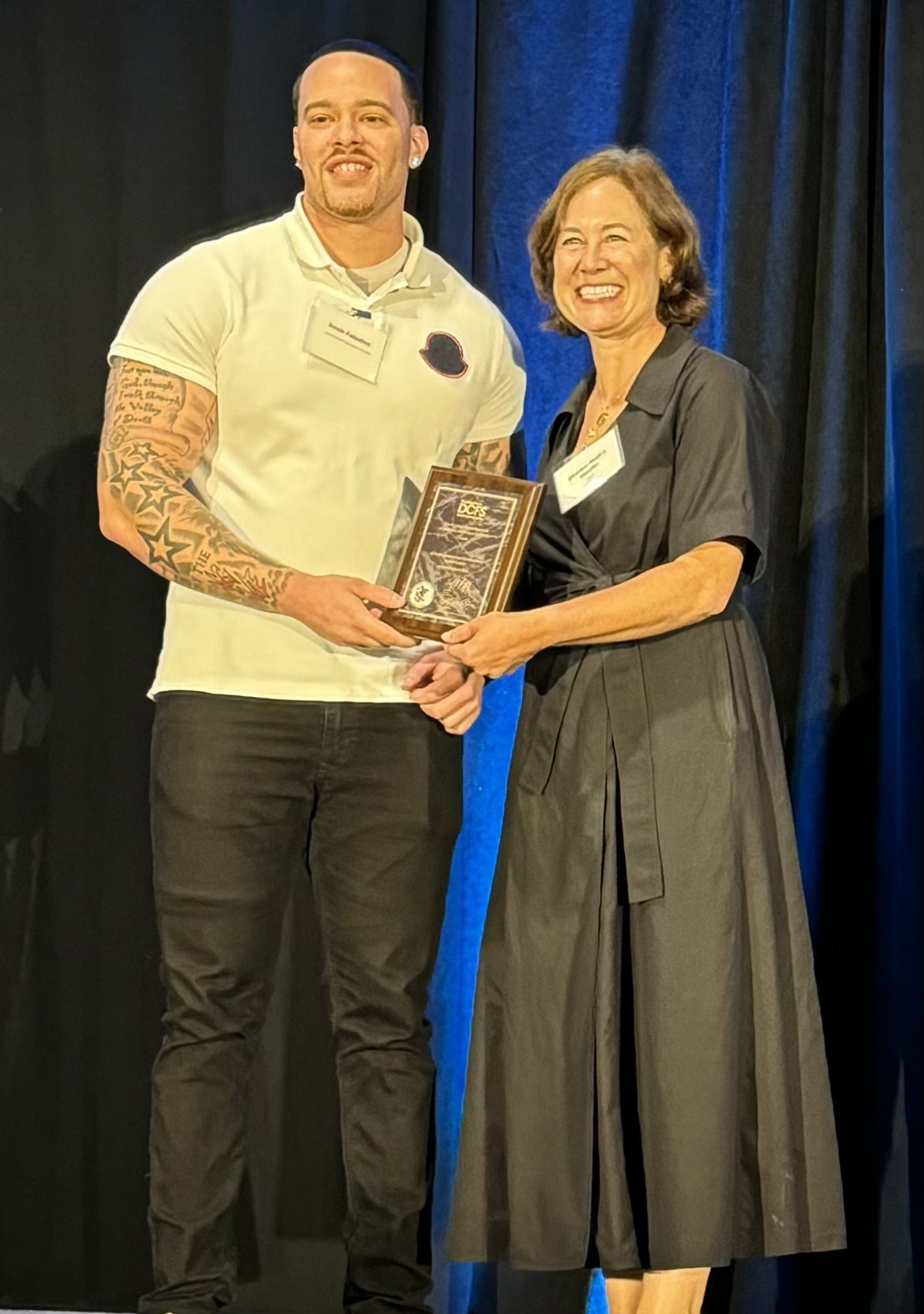 Devin Paladino accepting a framed award on stage