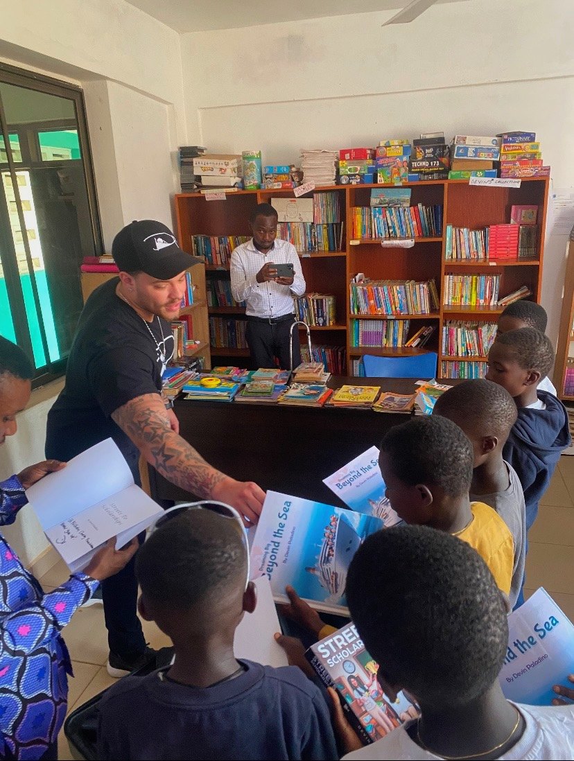 Devin Paladino handing books to pupils in a school library in Tema, Ghana