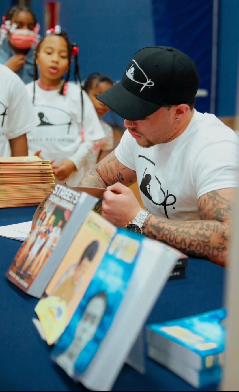 Devin Paladino signing copies of his books at a table while students wait in line