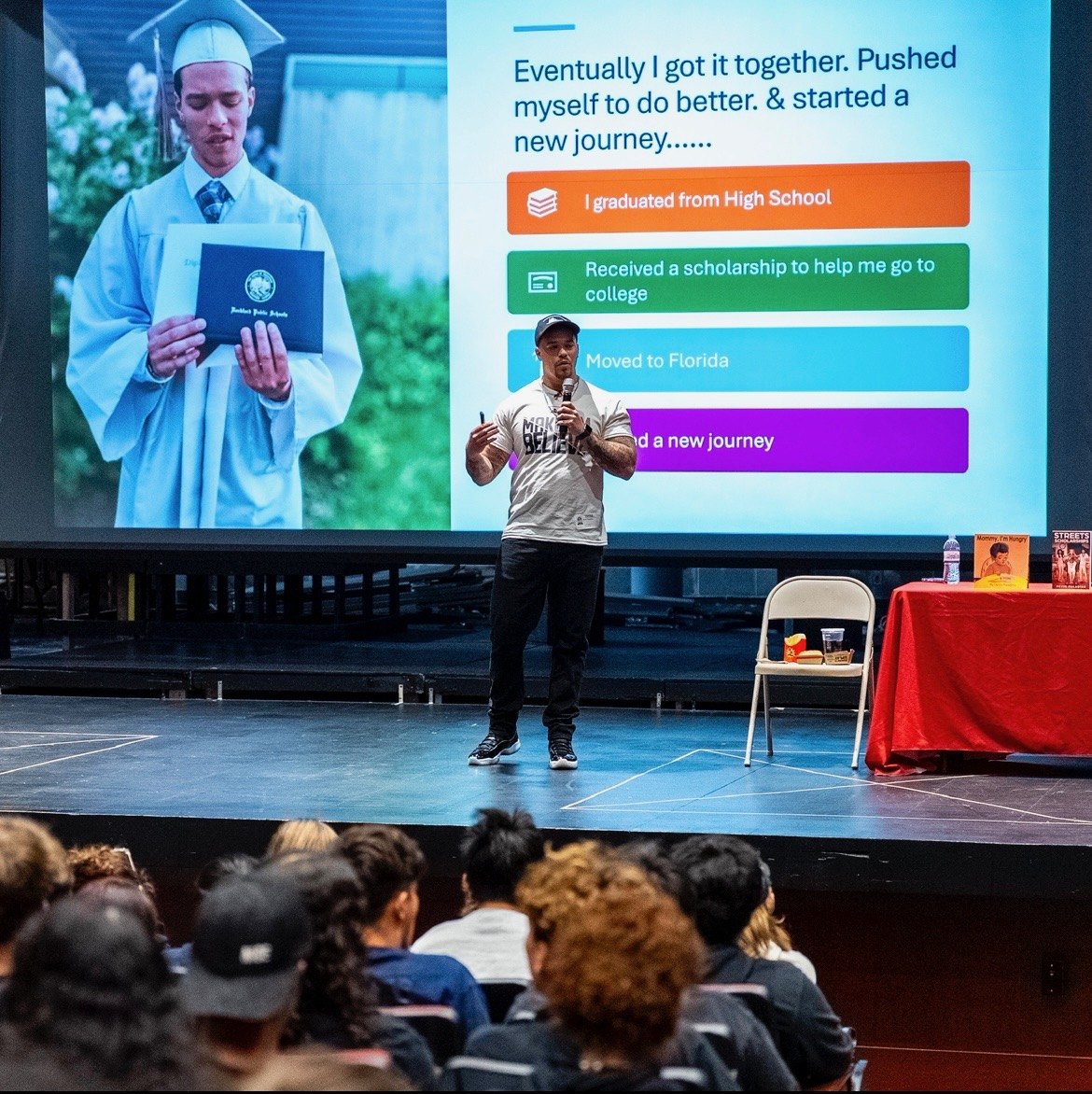 Devin Paladino on stage beside a projected slide showing his own graduation photograph and the steps that followed it
